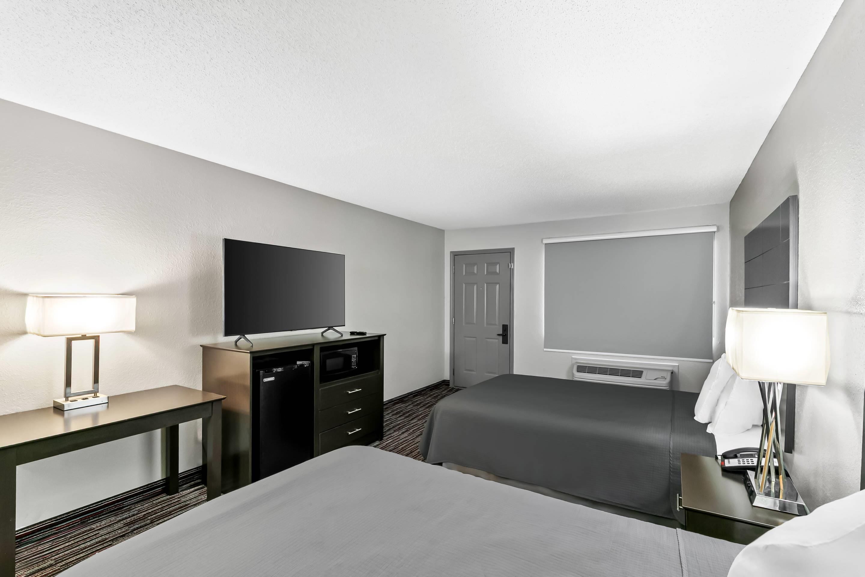 Une chambre d’hôtel avec un lit, un bureau avec une lampe, une télévision, un minibar et une porte.