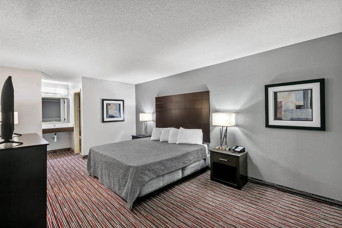 A hotel room with a large bed, bedside tables with lamps, a flat-screen TV, and a framed picture on the wall.