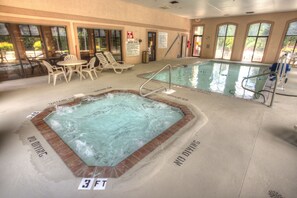 An indoor swimming pool with a hot tub, lounge chairs, and clear signage indicating no diving zones.