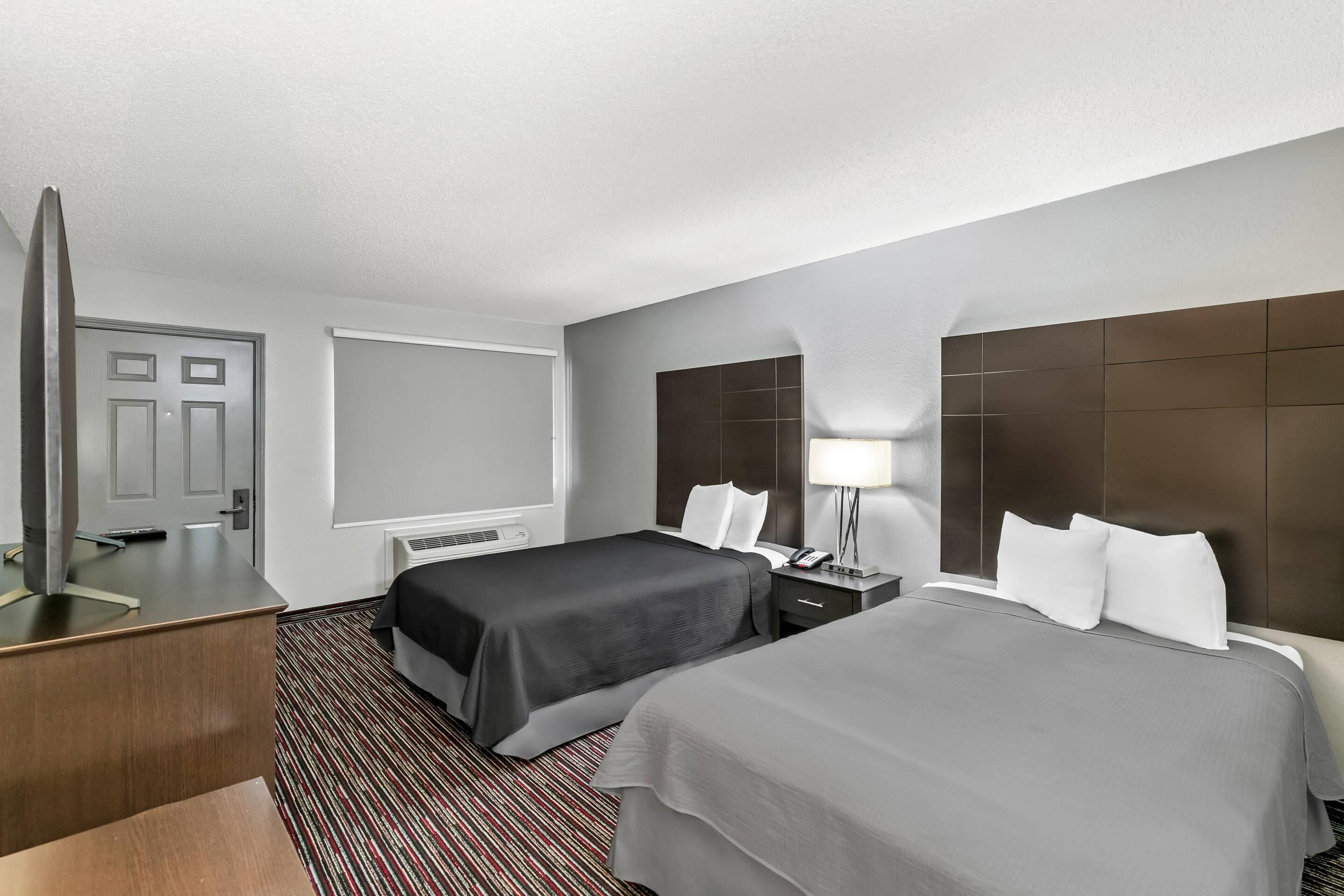 A hotel room with two beds, a desk, a mirror, and a TV.