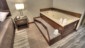 A hotel room with a large bathtub, a bedside table with a lamp, and a bed with a pillow. - Econo Lodge Helen (Helen)