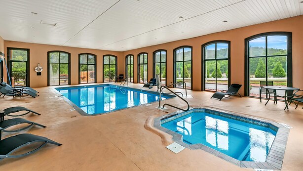 A large indoor swimming pool with multiple lanes, surrounded by sun loungers and a patio area with outdoor seating. - Econo Lodge Helen (Helen)