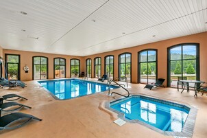 Una amplia piscina interior con varias pistas de natación, rodeada de tumbonas y un patio con mobiliario exterior.