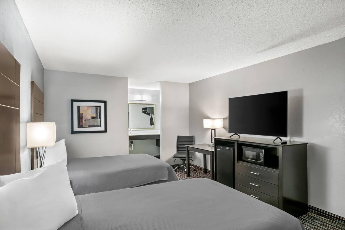 A hotel room with two beds, a desk, a flat-screen TV, a microwave, and a dresser.