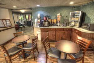 Un restaurante con mesas y sillas de madera, una estación de café y un refrigerador con bebidas.