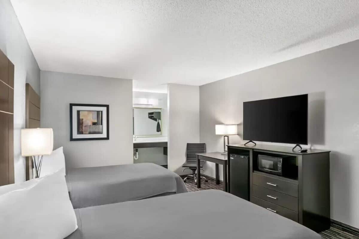 A hotel room with two beds, a desk, a television, a microwave, and a chair.