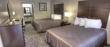 A hotel room with two beds, a desk, a mirror, a lamp, and a bathroom visible through an open door.
