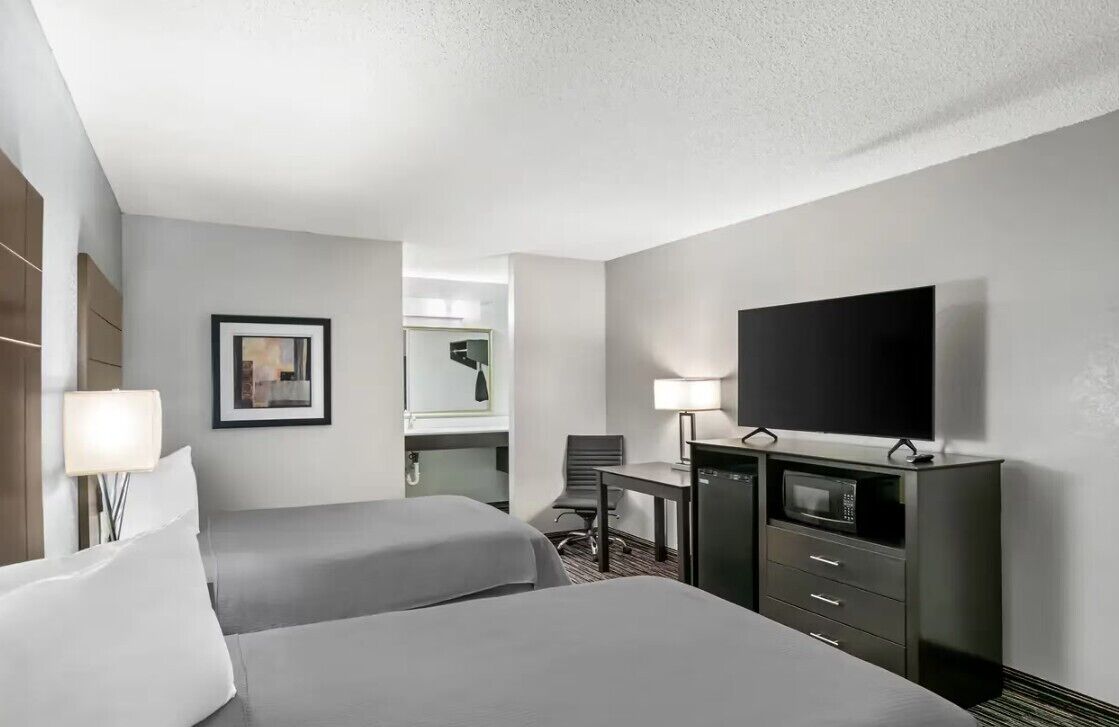 A hotel room with two beds, a desk, a television, a microwave, and a chair.