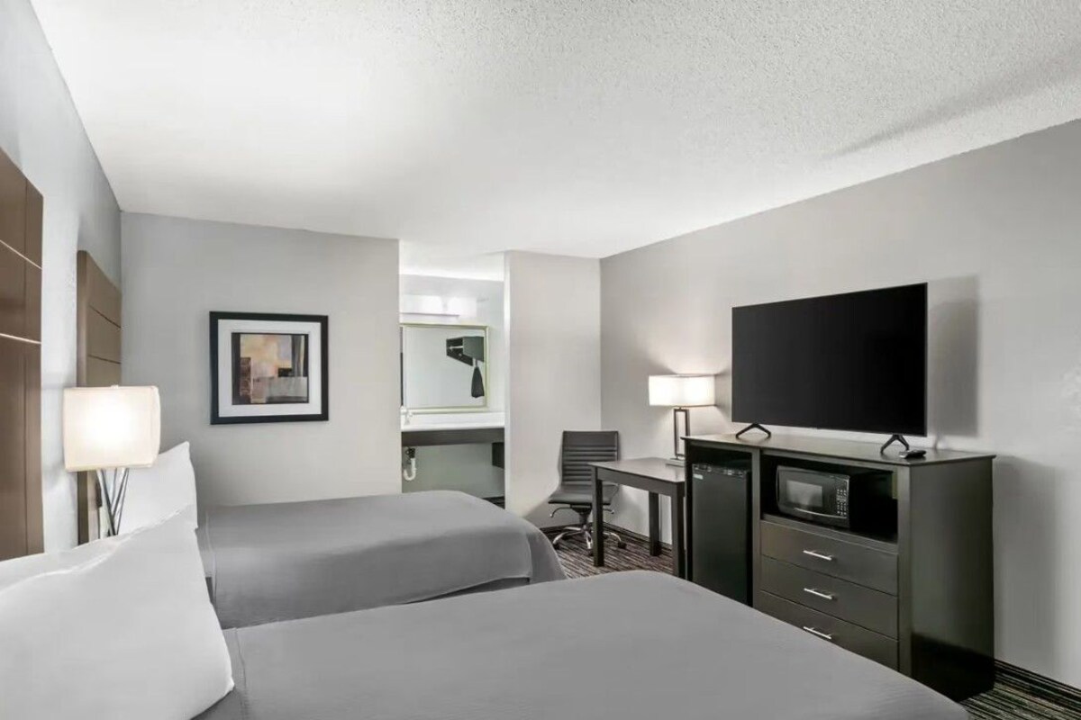 A hotel room with two beds, a desk, a television, a microwave, and a chair.