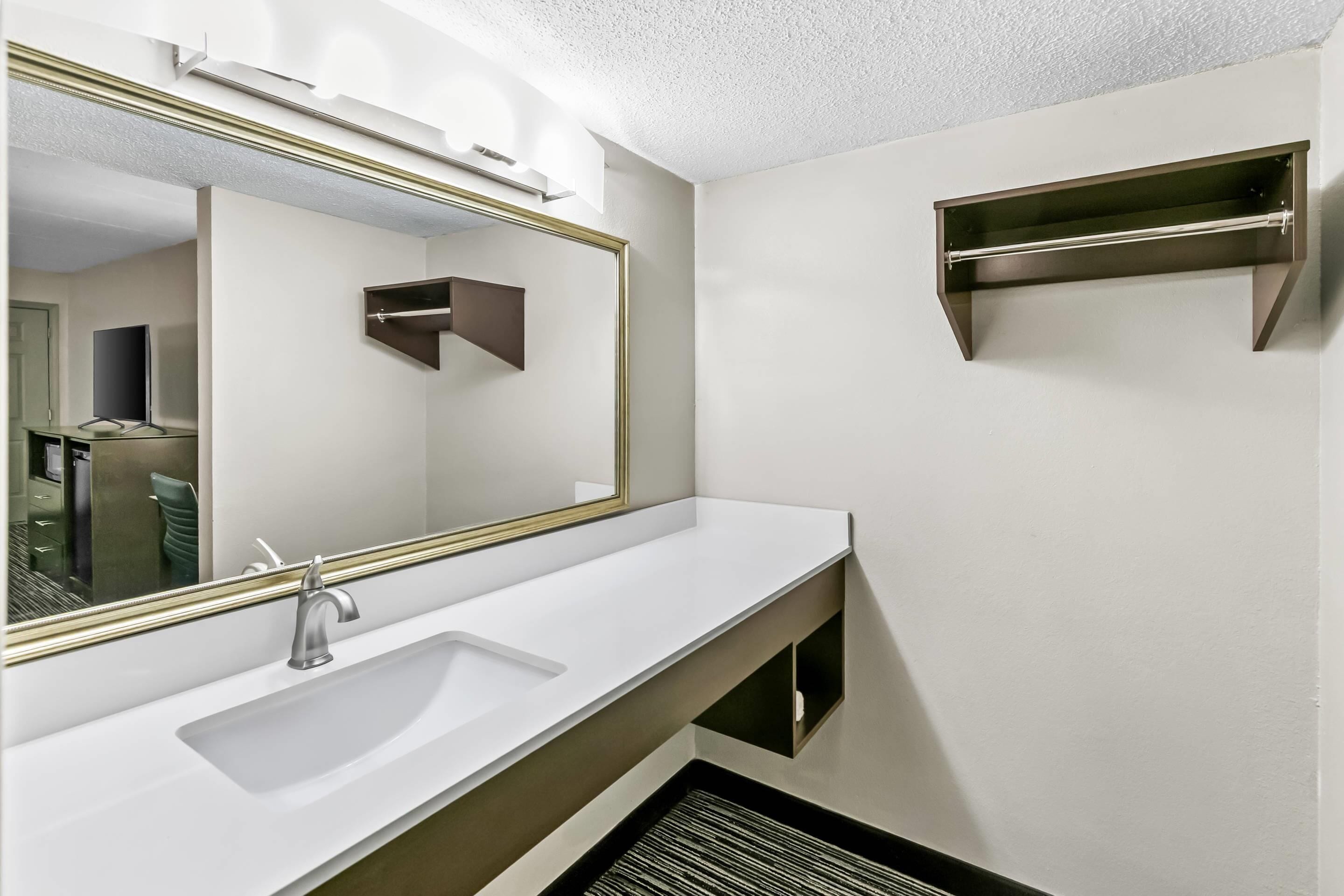 A modern bathroom with a white sink, a large mirror, and a built-in shelf.
