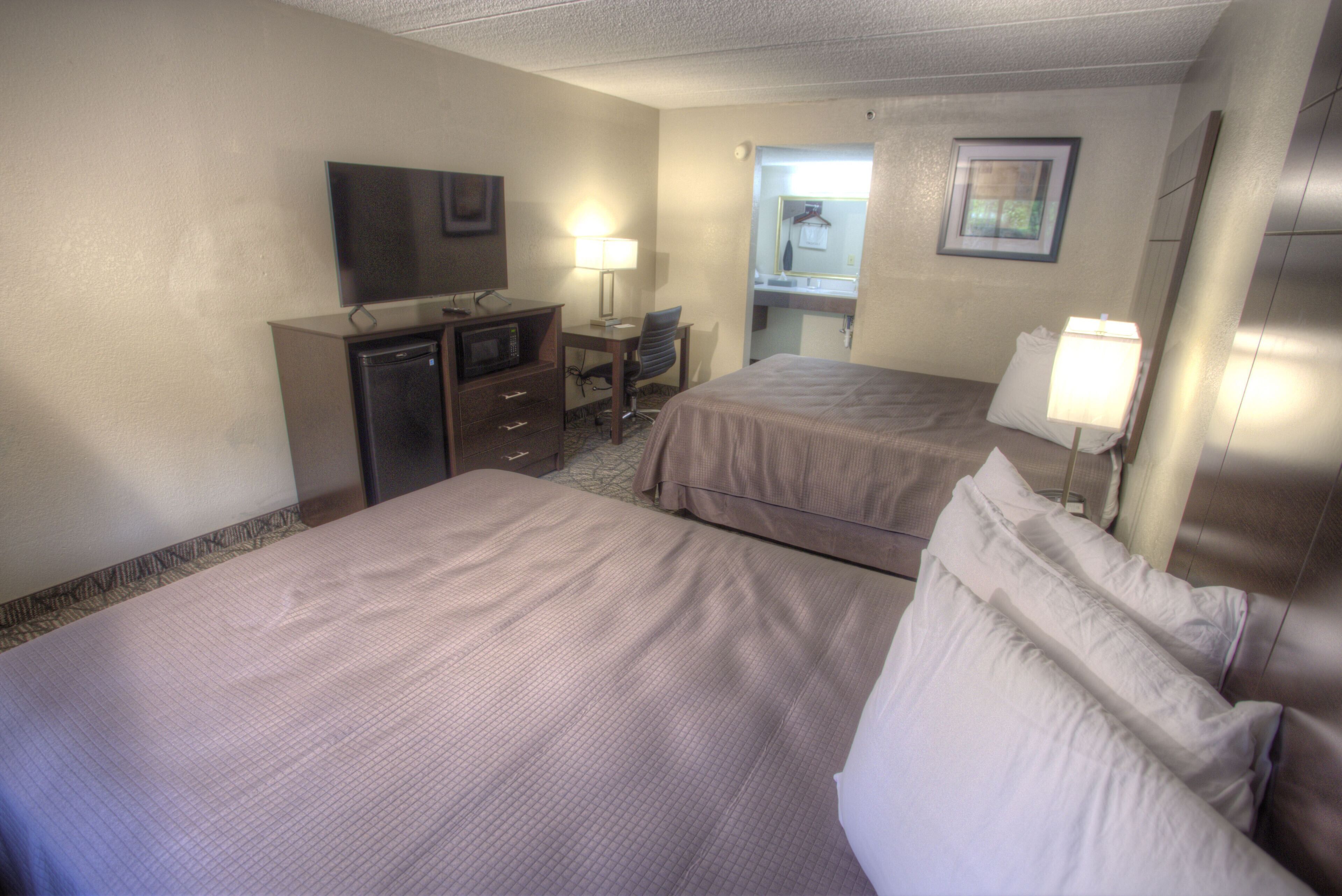 Een hotelkamer met twee bedden, een bureau met een computer, een televisie en een badkamer zichtbaar door een geopende deur.