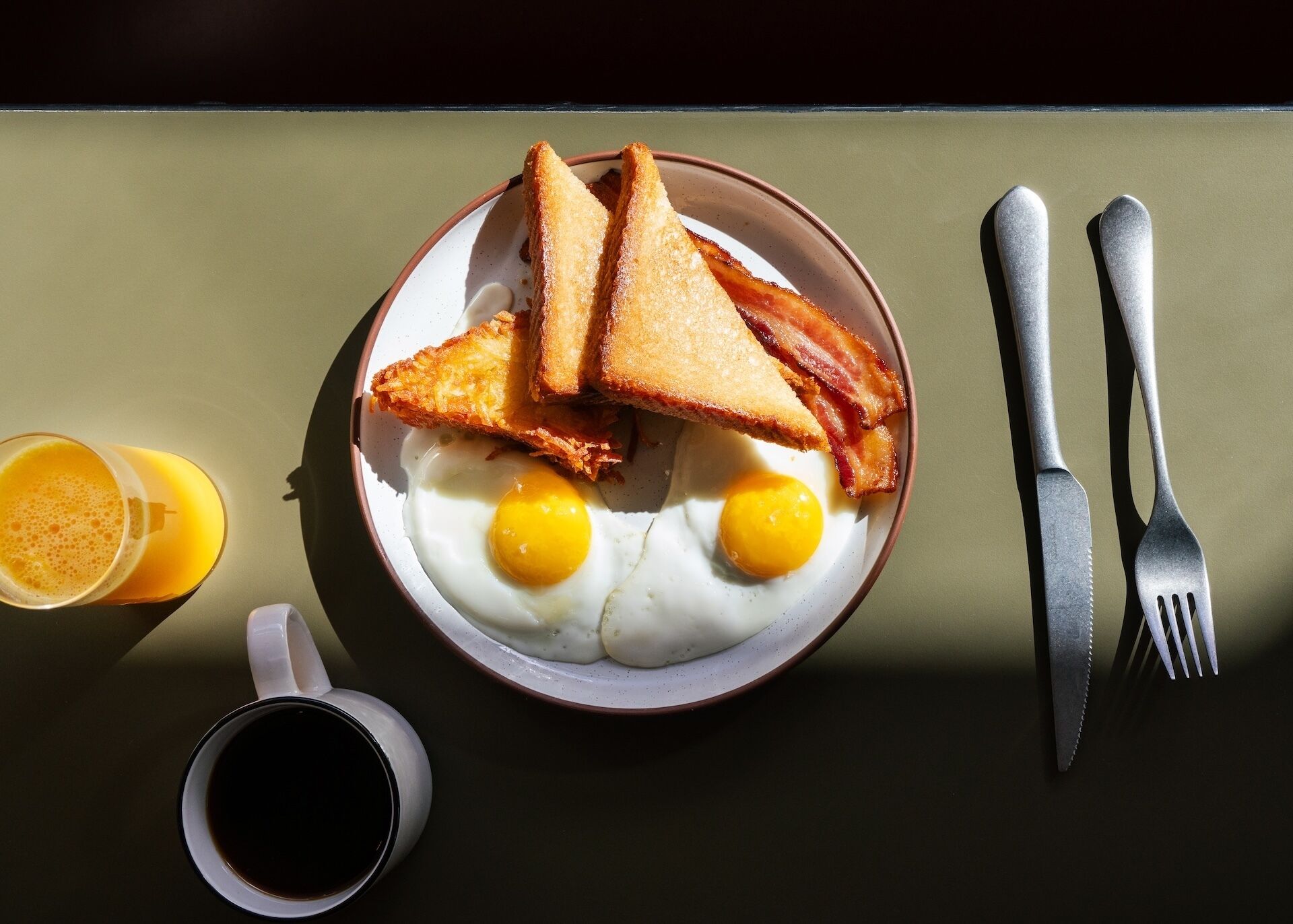 A breakfast plate with toast, bacon, and eggs, accompanied by a glass of orange juice and a cup of coffee.