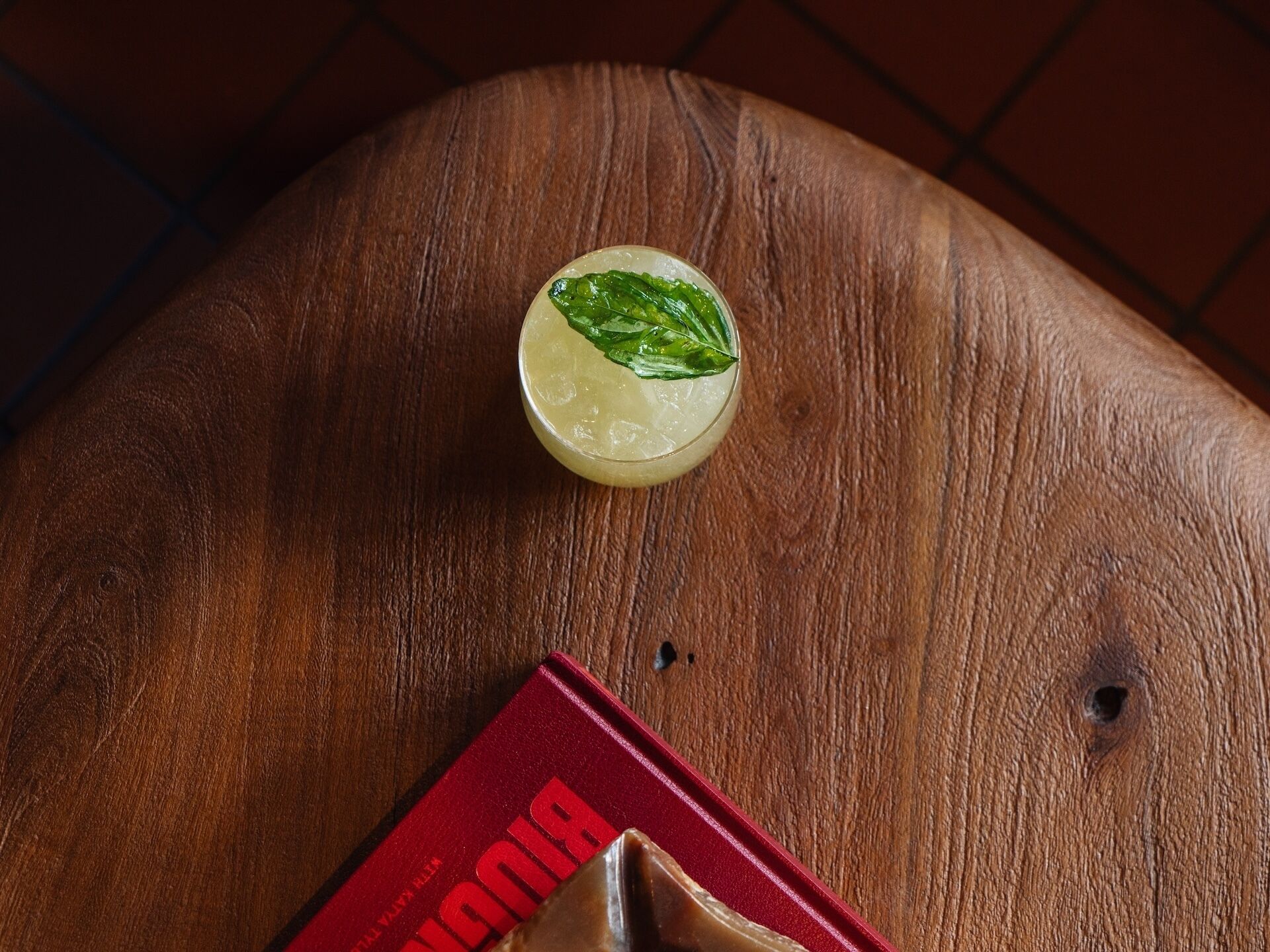 A glass of a light-colored beverage with a mint garnish on a wooden surface.