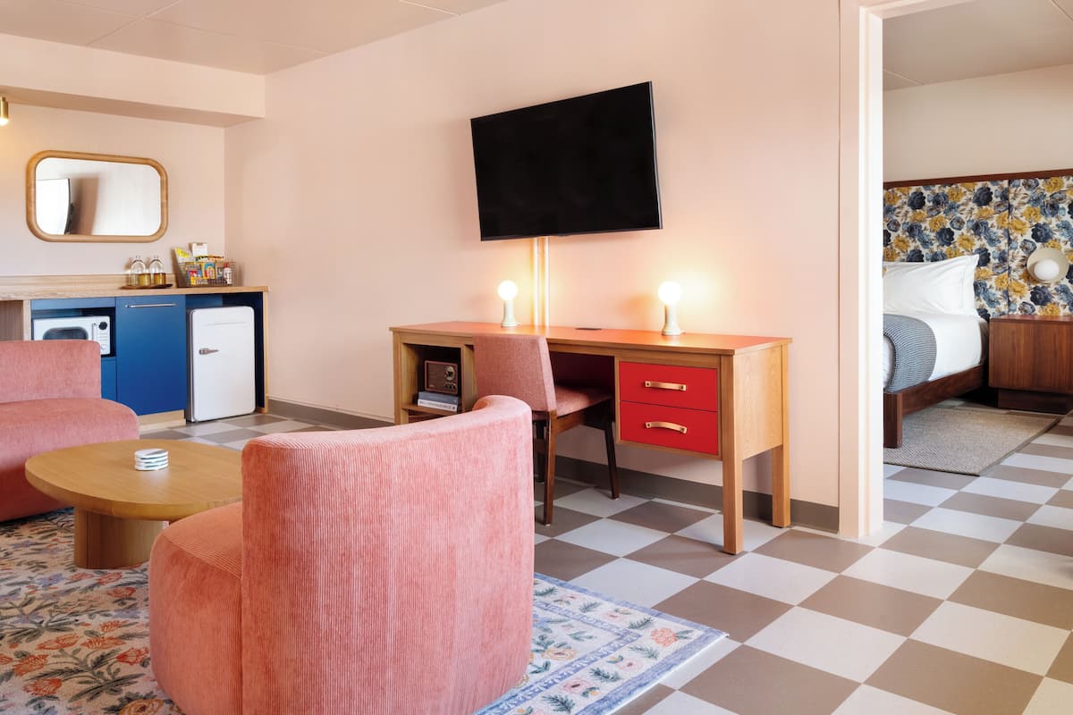 A hotel room with a kitchenette, a desk with a chair, a bed, and a small round table.