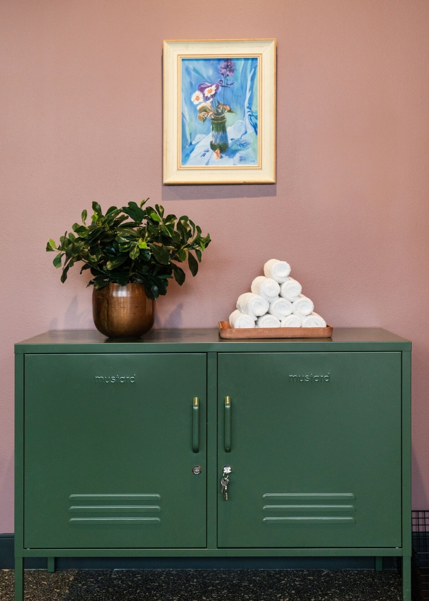 A green metal cabinet with a plant and a tray of rolled towels.