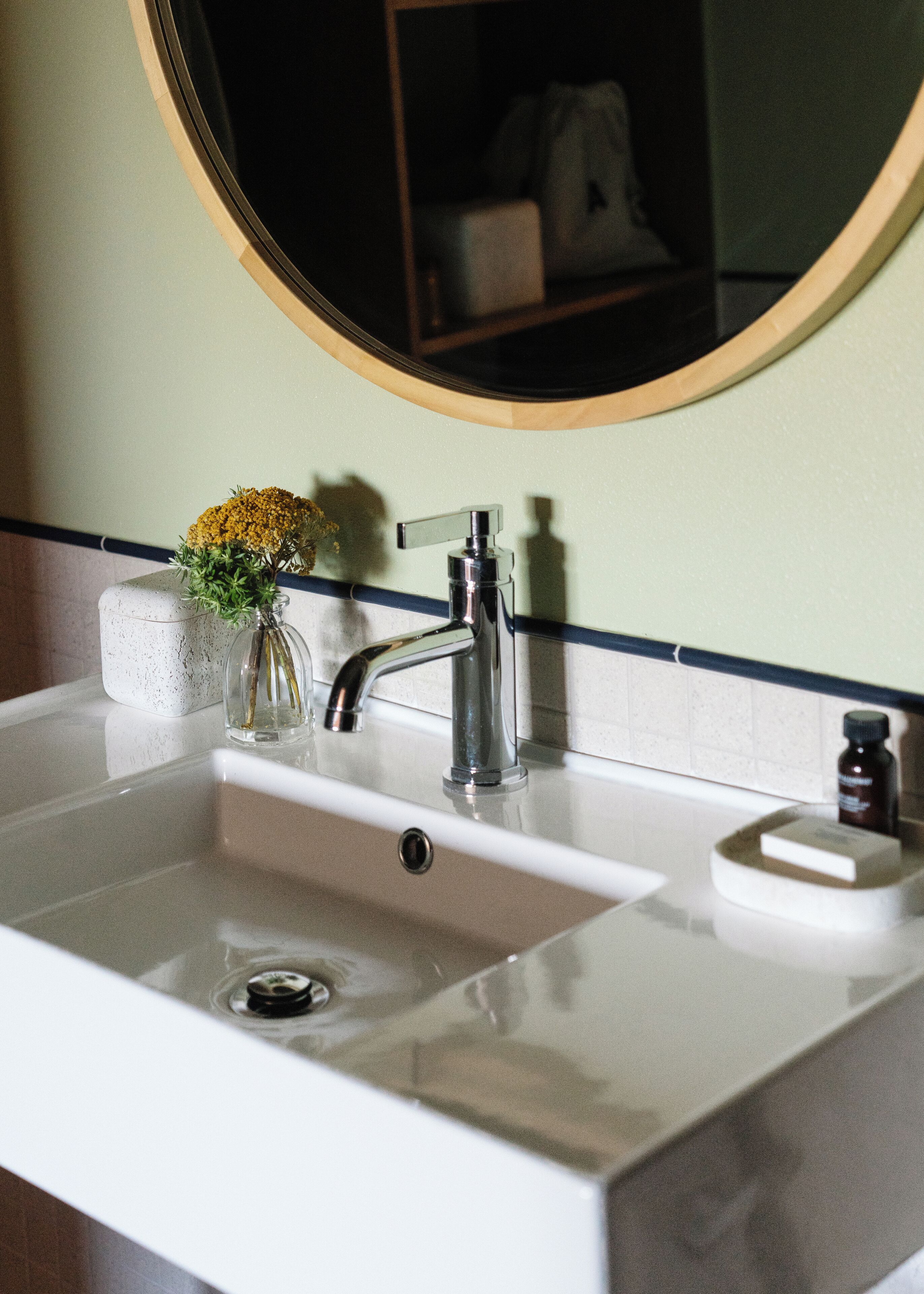 A bathroom sink with a mirror above it, a vase with flowers, and a soap dispenser.
