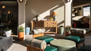 Un espacio al aire libre con luz solar, mobiliario de madera, plantas en macetas y un mueble de madera con cajones.