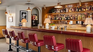 Una zona de bar con taburetes rojos, una estantería repleta de licores y una máquina de café.