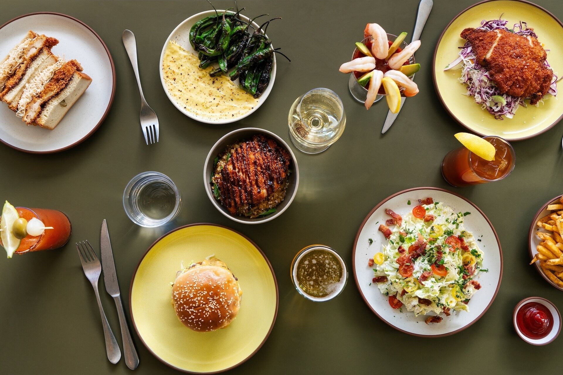 Una mesa dispuesta con diversos platos, como sushi, una hamburguesa, ensalada y un cóctel de camarones.