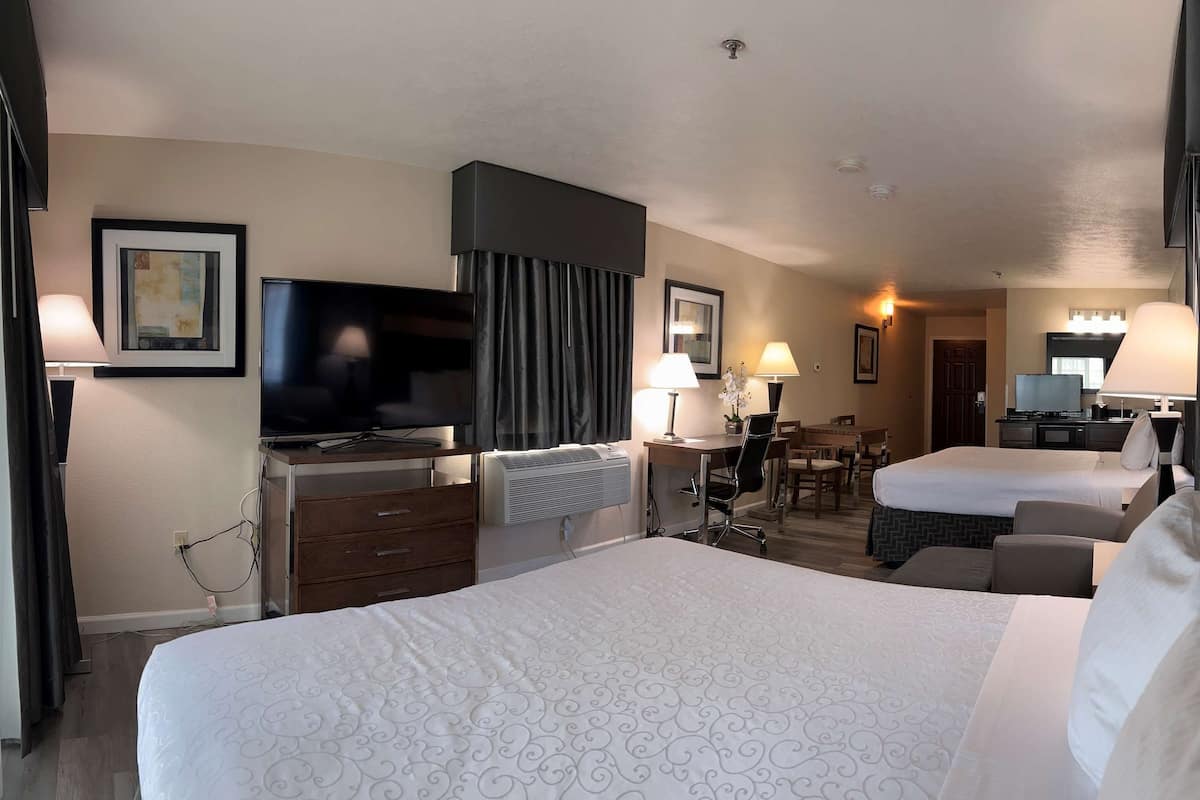 A hotel room with two beds, a desk, a TV, and a bathroom.