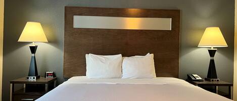 A hotel room with a large bed, two bedside tables with lamps, a clock, and a phone on one of the tables.