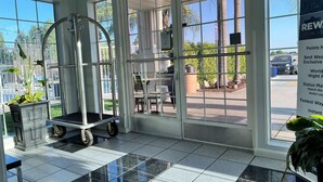 A hotel lobby with a tiled floor, a cart, and a large window with a view of the outside. - Best Western Americana (Dinuba)