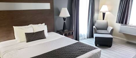 A hotel room with a large bed, a desk with a lamp, a chair, and a window with curtains.
