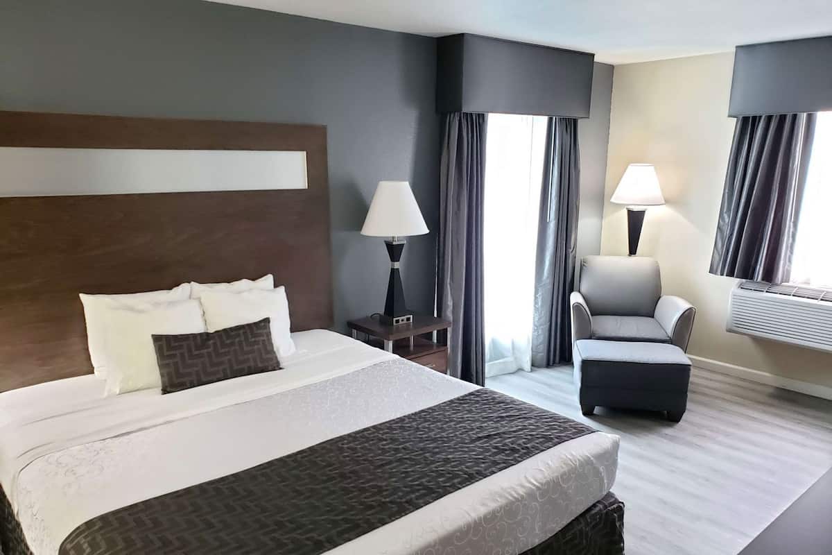 A hotel room with a large bed, a chair, a desk, and a window with curtains.