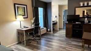 A hotel room with a desk, chair, lamp, air conditioning unit, and a television. - Best Western Americana (Dinuba)