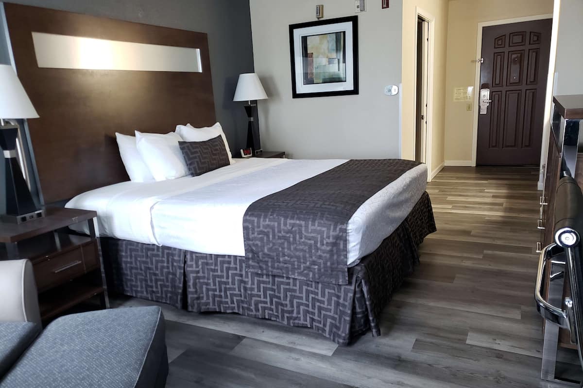 A hotel room with a large bed, bedside tables, a chair, a desk, and a door.