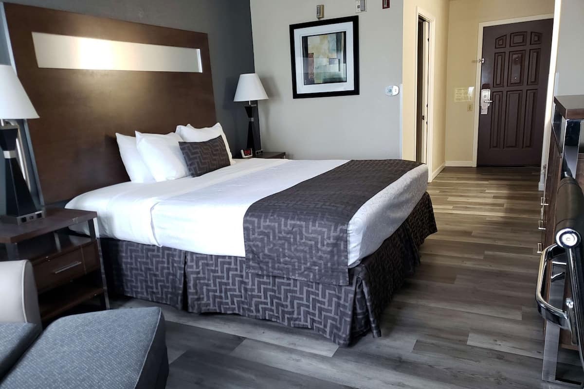 A hotel room with a bed, bedside table, lamp, and a door leading to another room.