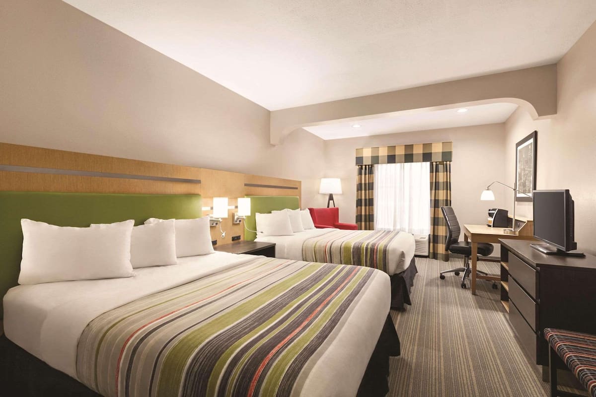 A hotel room with two beds, a desk, a chair, a television, and a window with curtains.