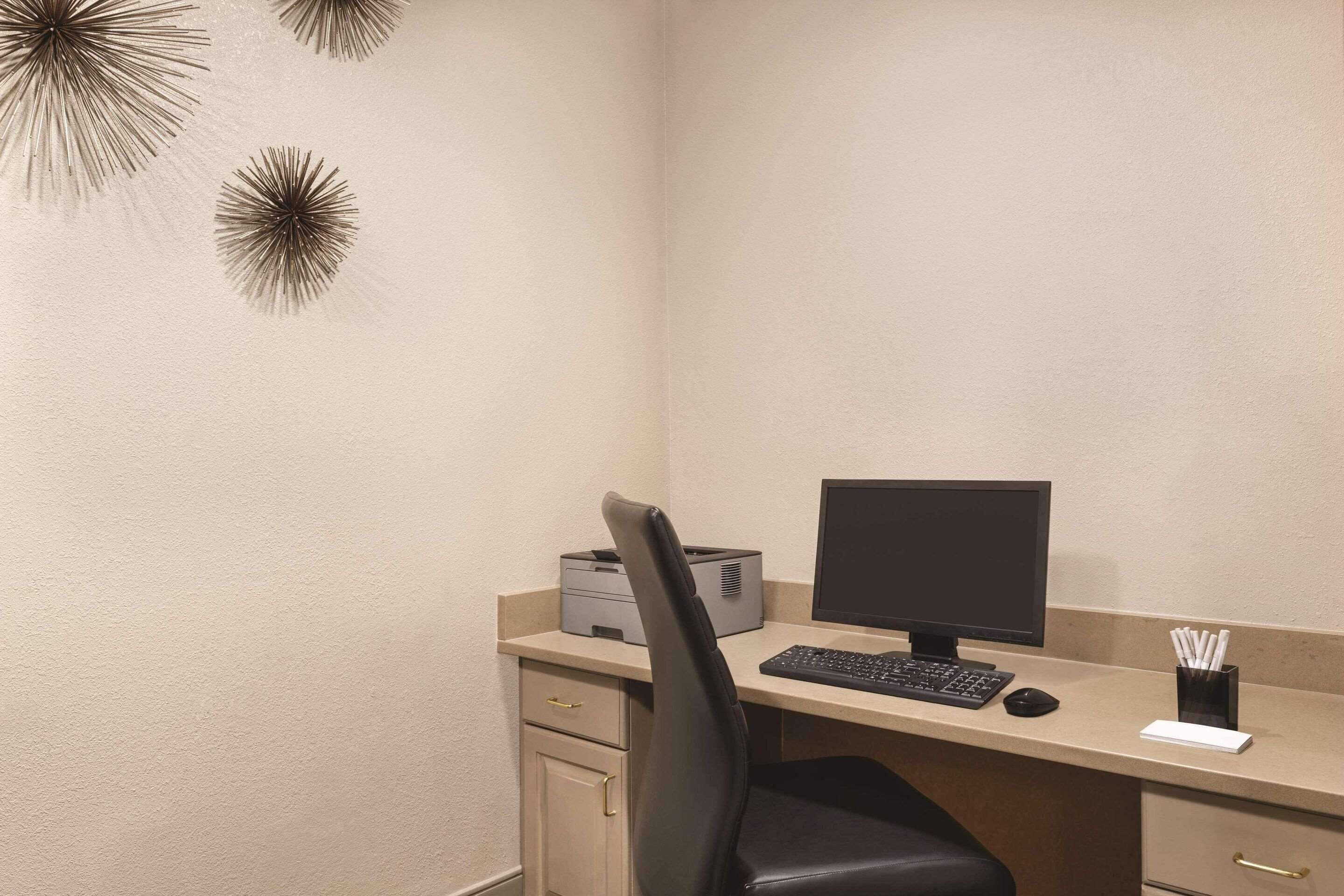 A small office with a desk, chair, computer, printer, and a wall decoration.