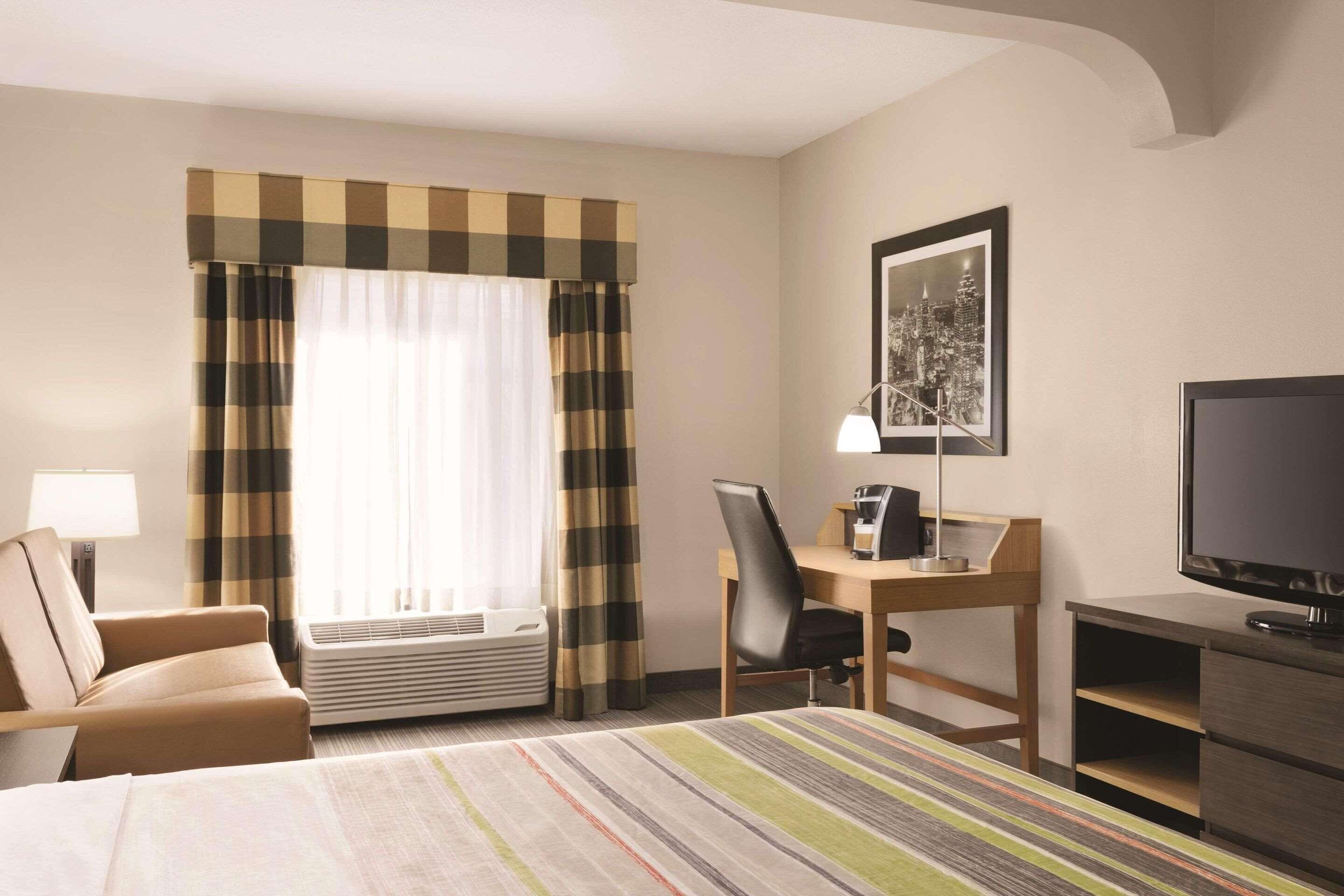 A hotel room with a bed, a desk with a chair, a television, and a window with curtains.