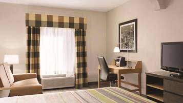 A hotel room with a bed, a desk with a chair, a television, and a window with curtains.