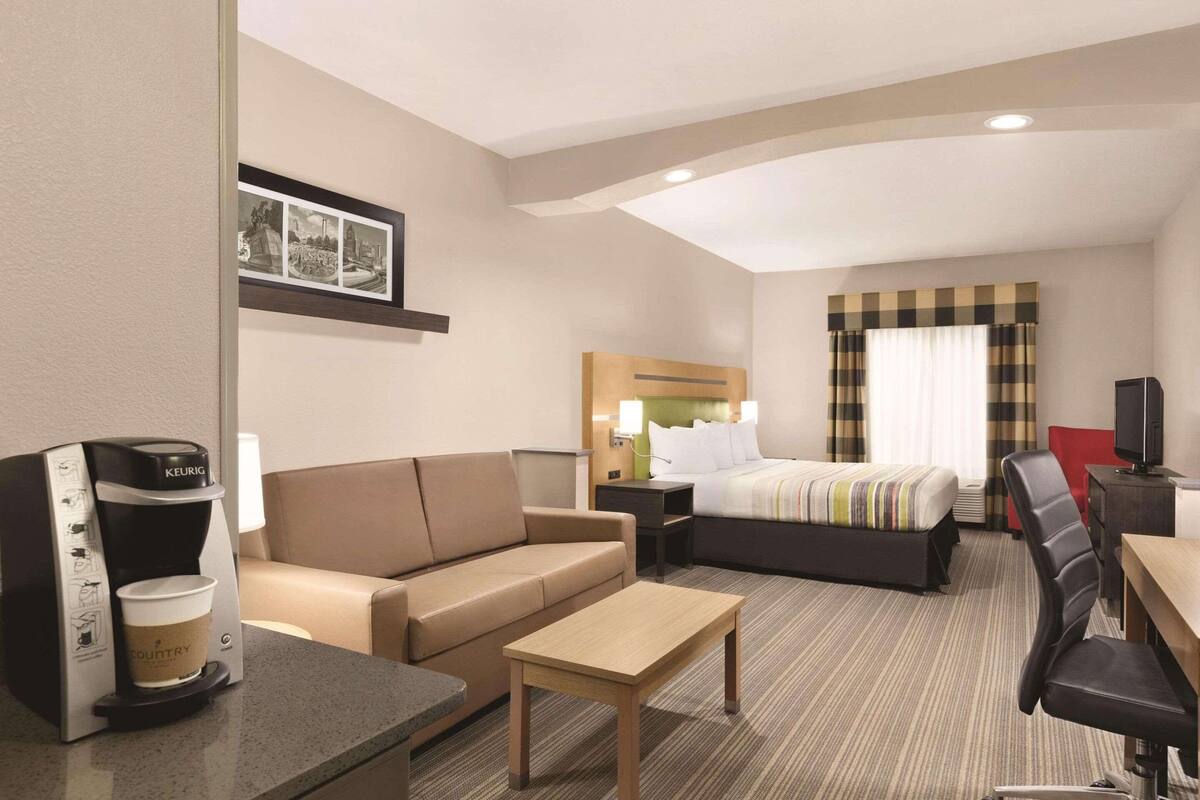 A hotel room with a bed, a sofa, a coffee maker, a TV, and a desk.