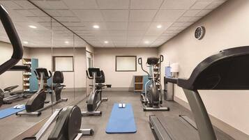 A gym with cardio machines, a blue mat, and a mirror.