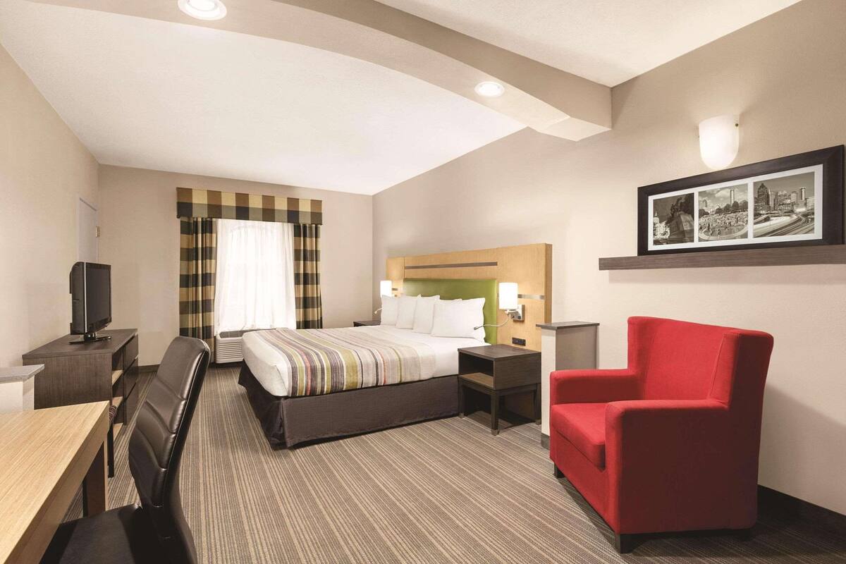 A hotel room with a bed, a desk, a chair, a TV, and a framed picture on the wall.
