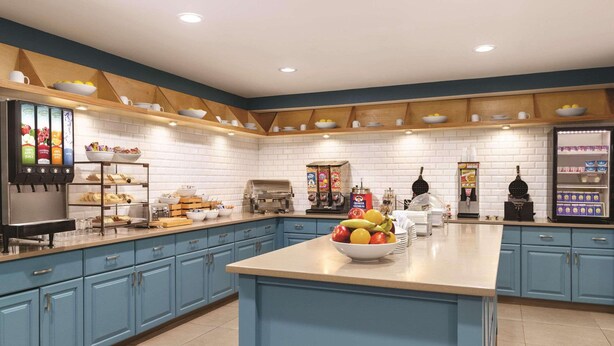 A modern kitchen with blue cabinets, a central island with fruit, a coffee station, and a refrigerator. - Country Inn & Suites by Radisson, Griffin, GA (Griffin)