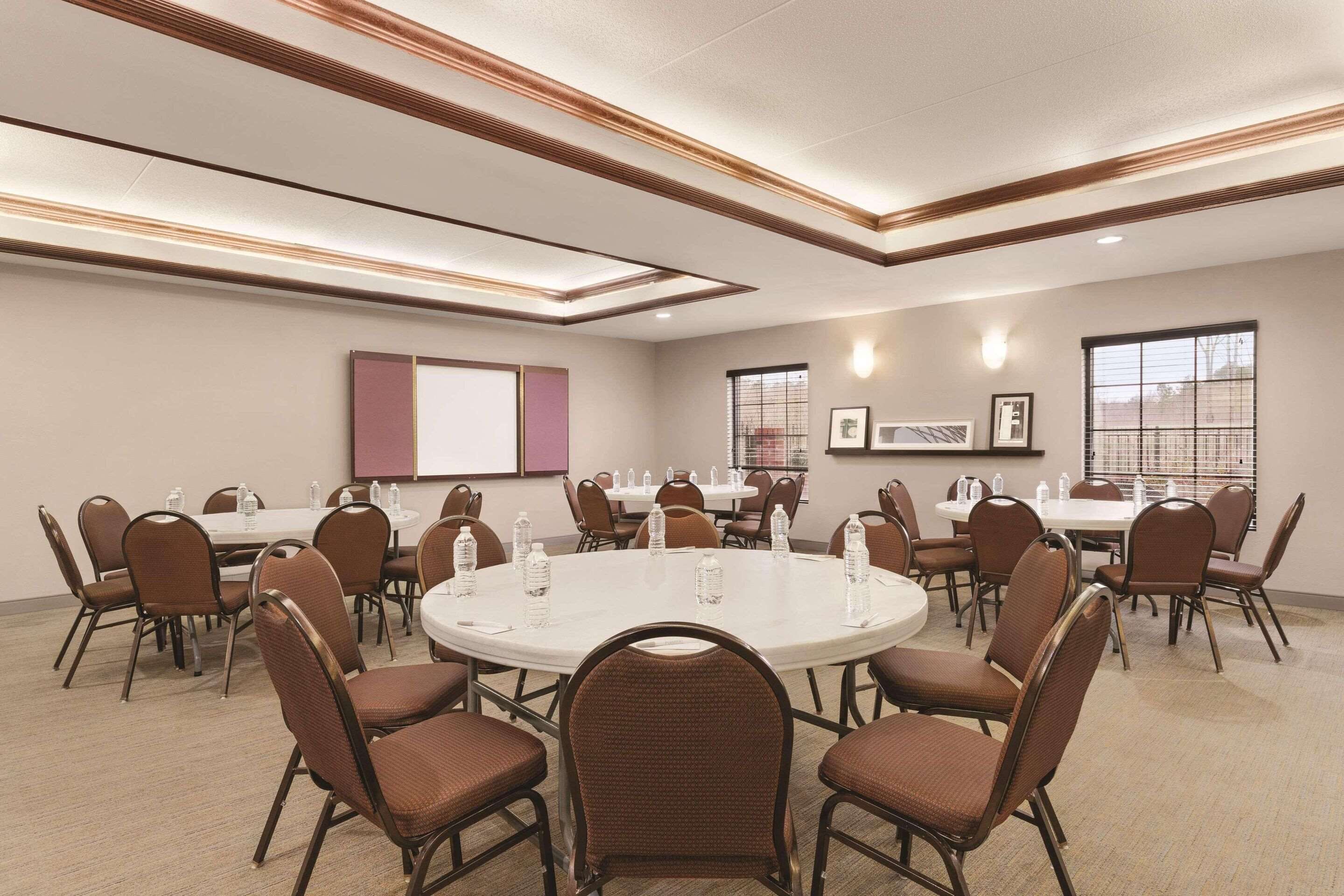 Une salle de conférence dotée de tables et de chaises rondes, ainsi que de bouteilles d’eau et d’écrans de présentation.