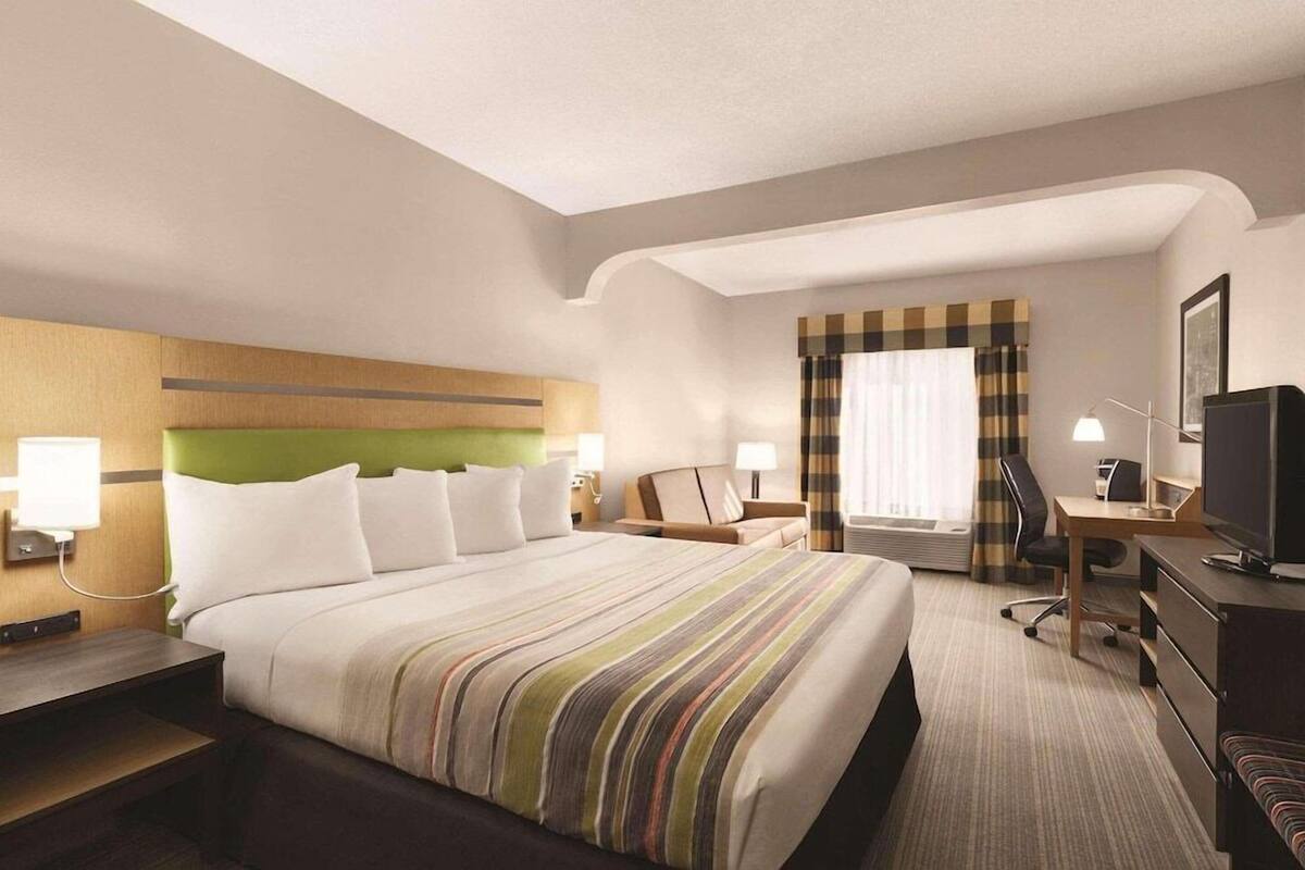 A hotel room with a large bed, a desk, a chair, a television, and a window with curtains.