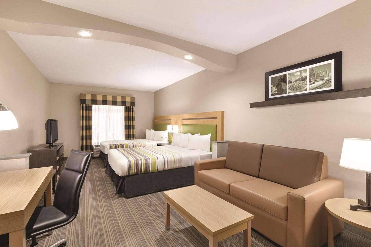 A hotel room with a bed, a sofa, a desk, a chair, and a television.
