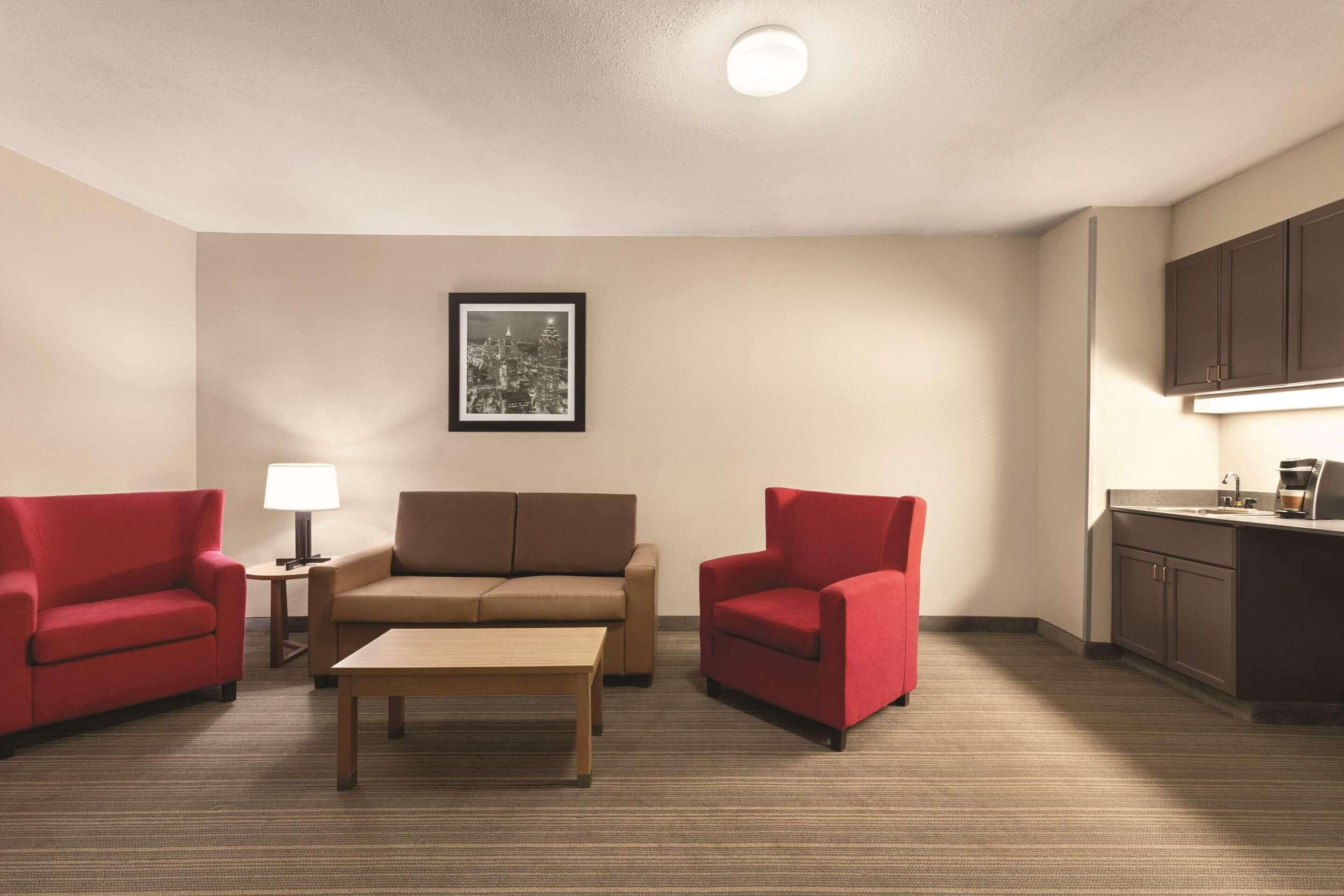 Una sala compacta con un sofá, dos sillones rojos, una mesa de centro, una lámpara y un cuadro enmarcado en la pared.
