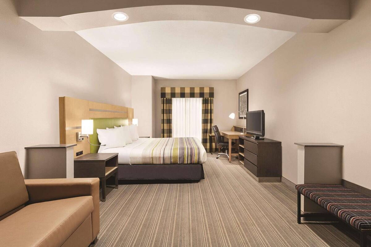 A hotel room with a bed, a desk, a chair, a TV, and a bench.