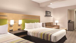 A hotel room with two beds, a desk, a chair, and a small kitchenette.
