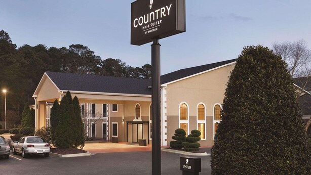 A Country Inn & Suites by Radisson building with a signboard, parking area, and well-maintained landscaping.