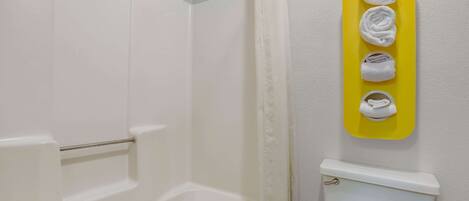 Une salle de bain avec une baignoire blanche, des toilettes et un rideau de douche. On y trouve un porte-serviettes jaune sur lequel sont suspendues trois serviettes.