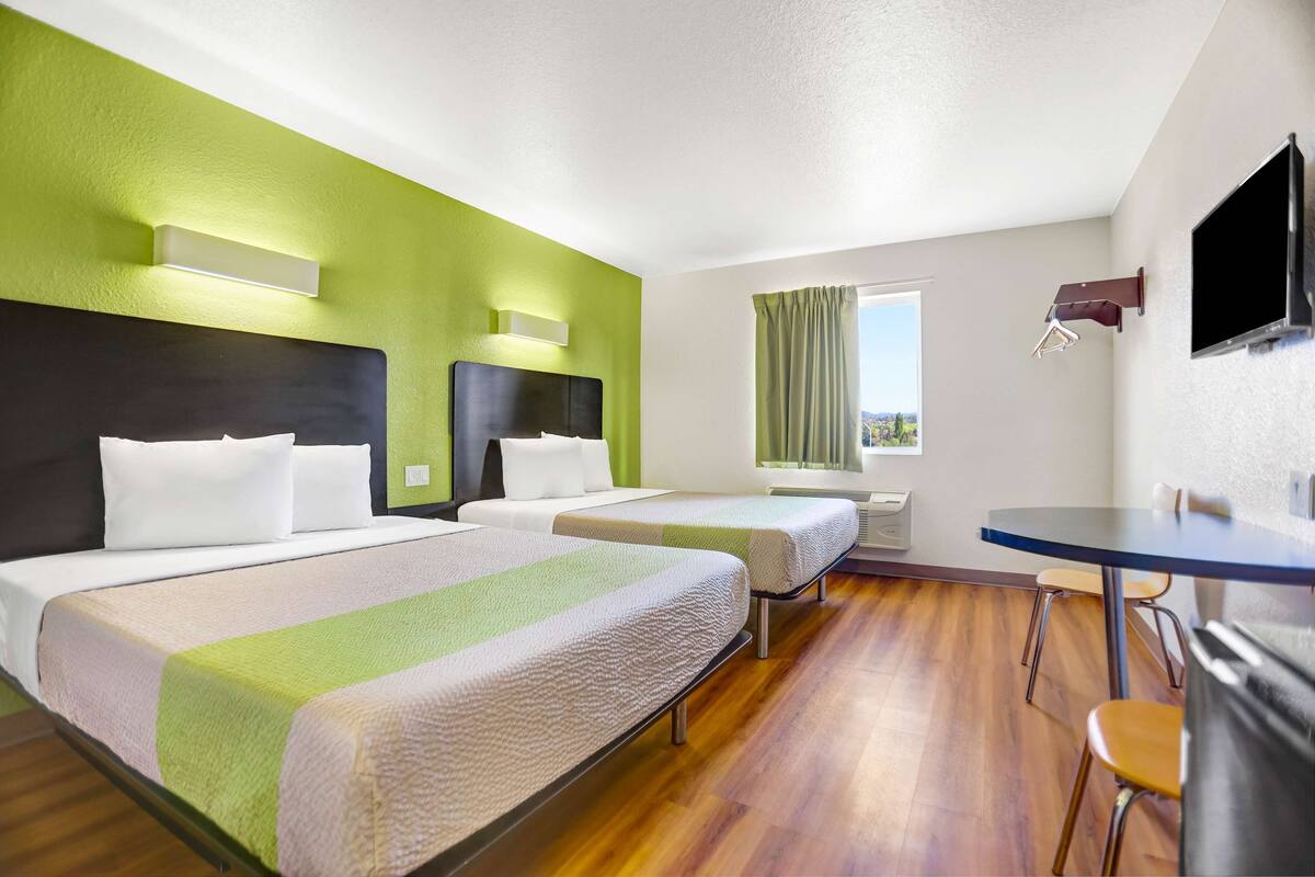 A hotel room with two beds, a dining table, and a TV.