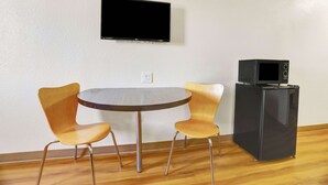A room with a round table, two chairs, a flat-screen TV mounted on the wall, and a black refrigerator with a microwave on top. - Motel 6 Silver City, NM (Silver City)