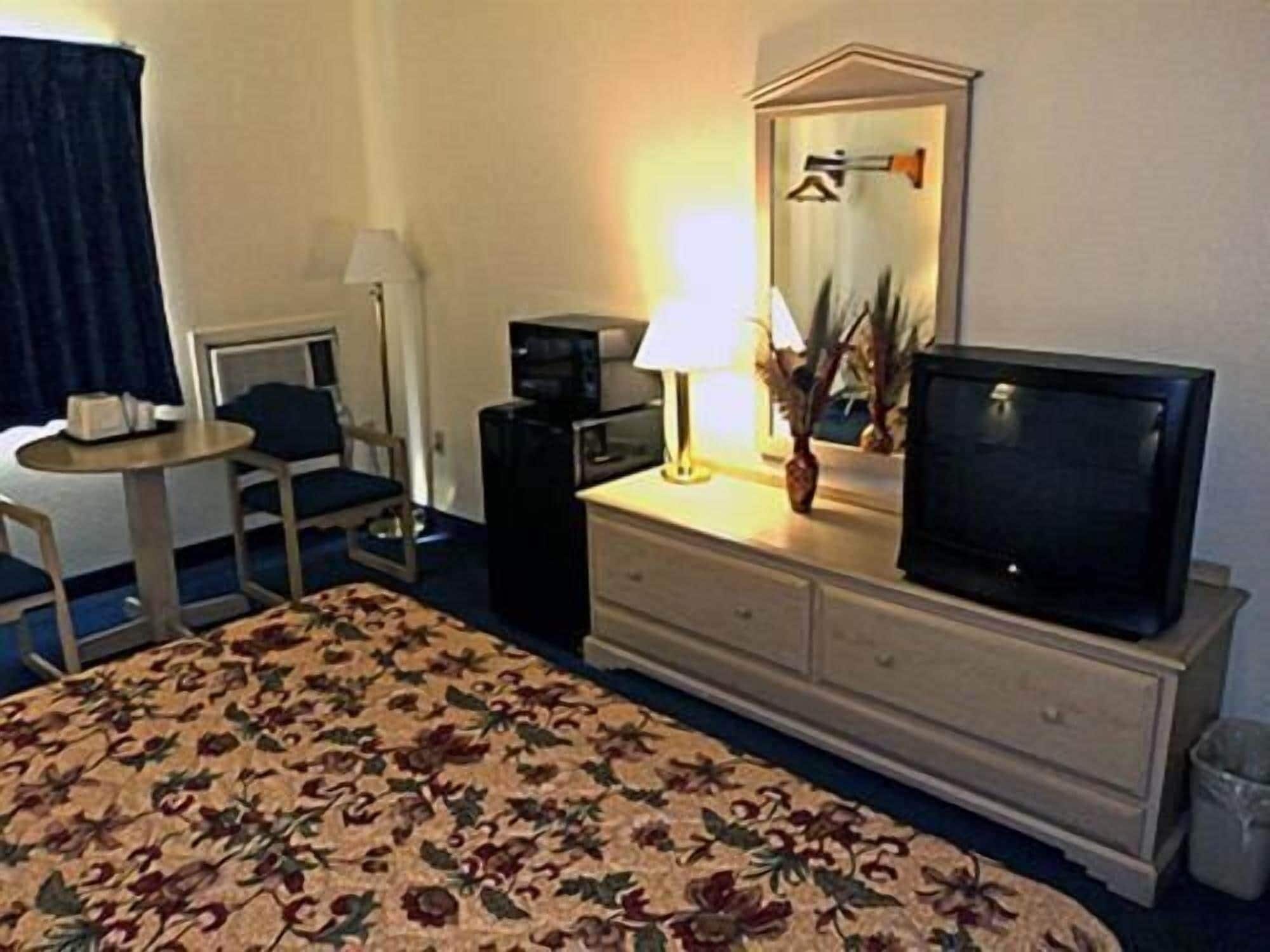 A hotel room with a bed, a desk, a chair, a television, a dresser, and a lamp.